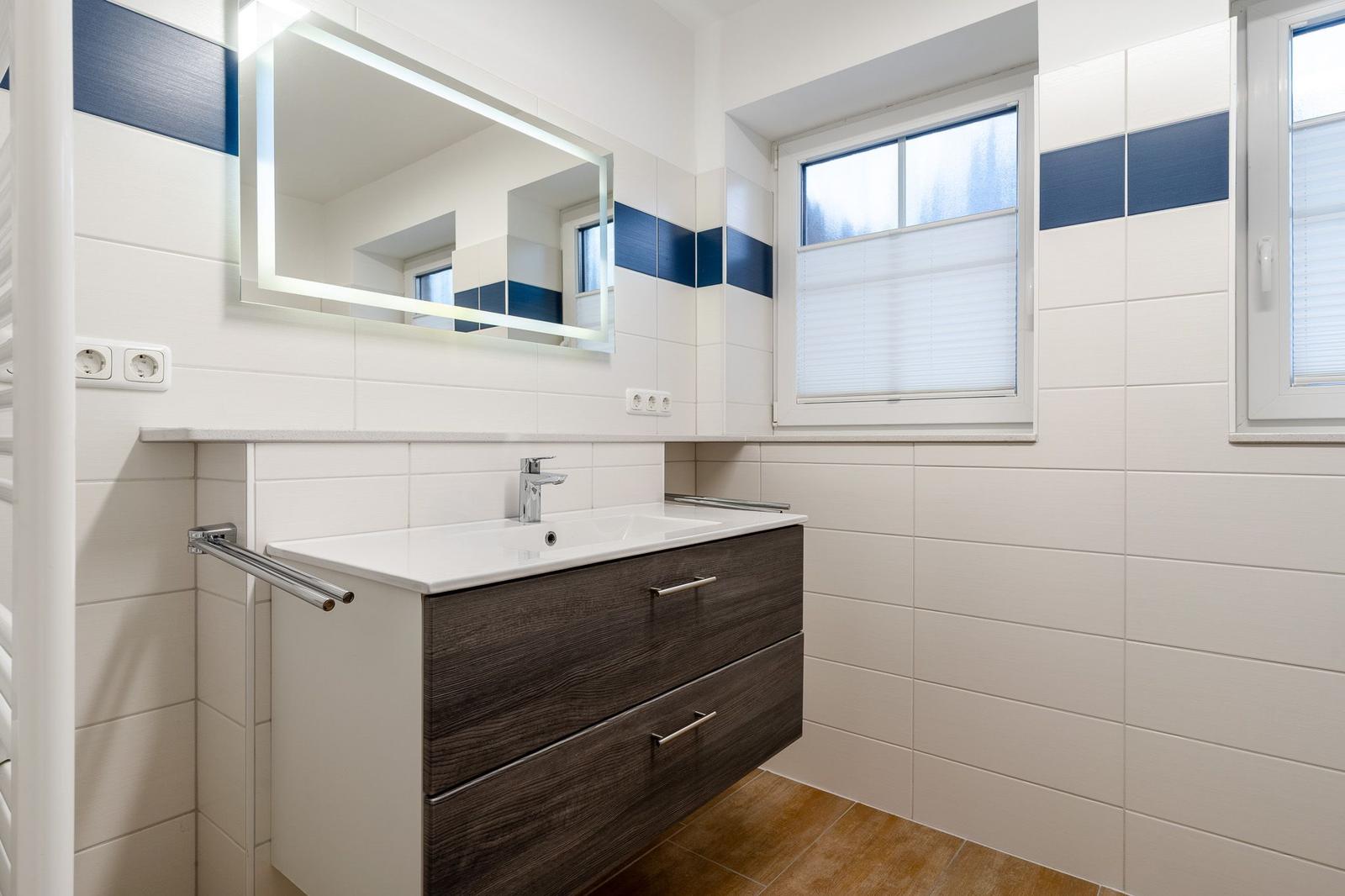 Badezimmer mit Waschtisch, Spiegel und Fenster.