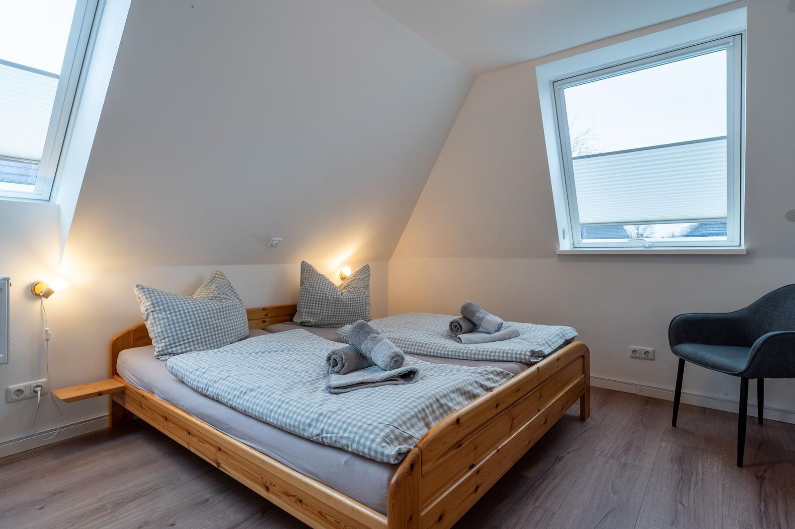 Schlafzimmer mit Dachschräge, Holzbett, Fenster und Sessel.