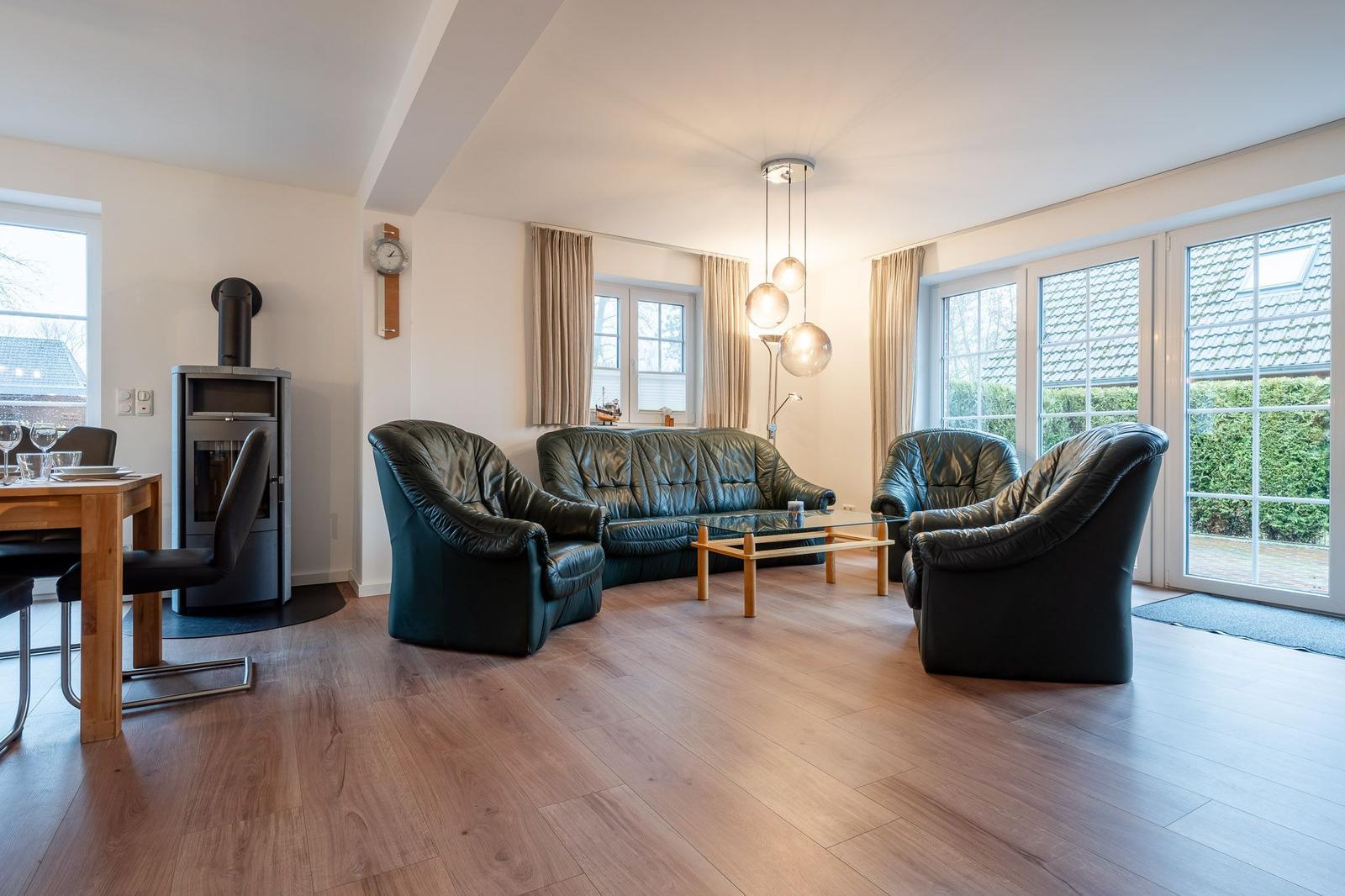Wohnzimmer mit Ledersofa, Sesseln, Holzboden und Fenstern.