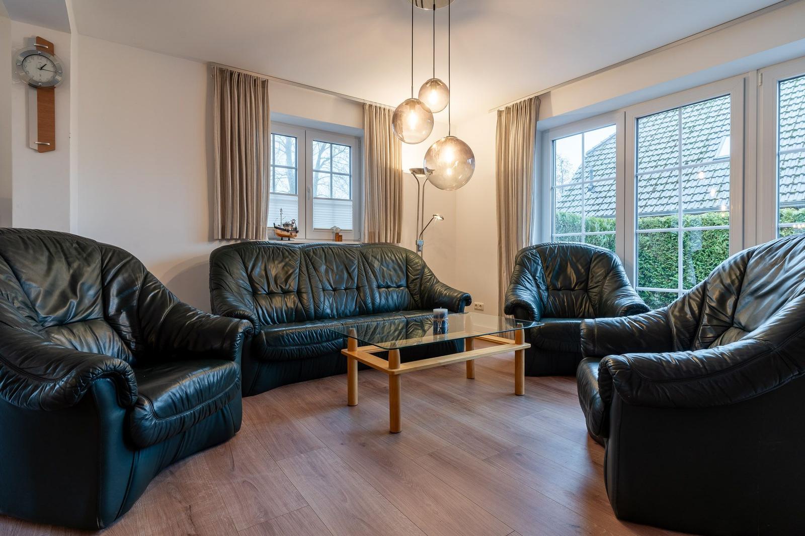 Wohnzimmer mit schwarzen Ledermöbeln, Glas-Tisch und großen Fenstern.