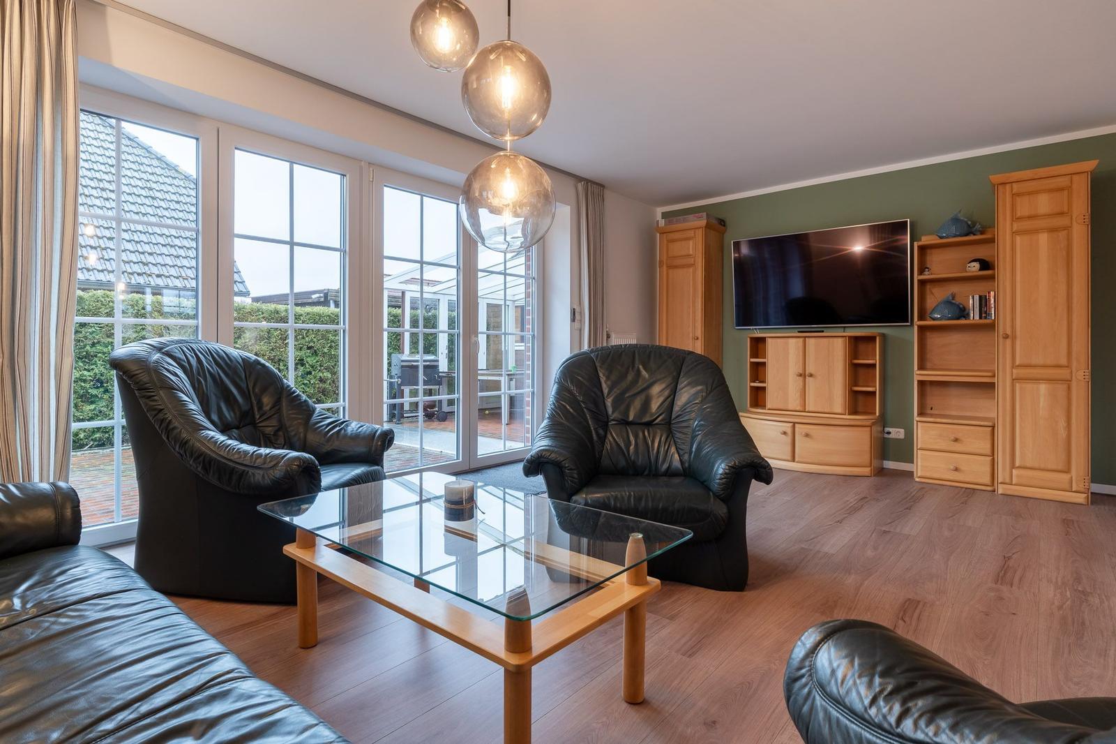Wohnzimmer mit zwei Ledersesseln, Glas-Tisch und Fernseher an Wand.