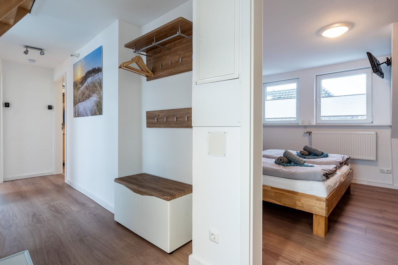 Schlafzimmer mit Bett und Fenstern. Flur mit Kleiderständer und Bild.