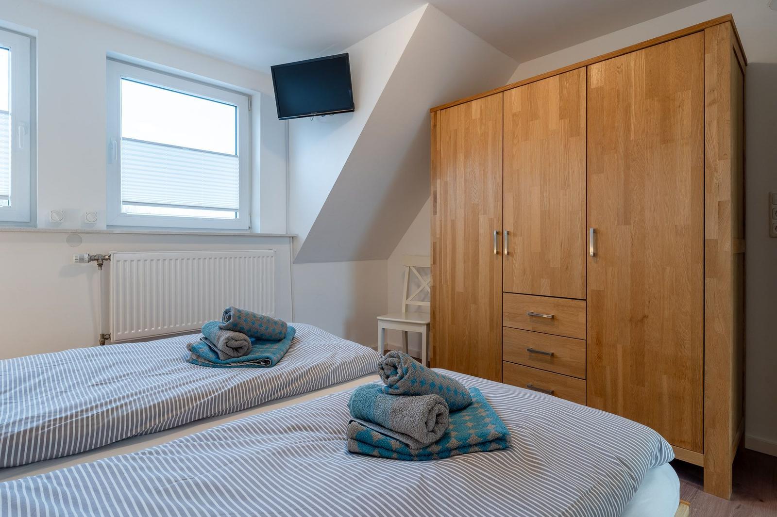Zwei Betten mit Handtüchern, Holzschrank und TV an der Wand.