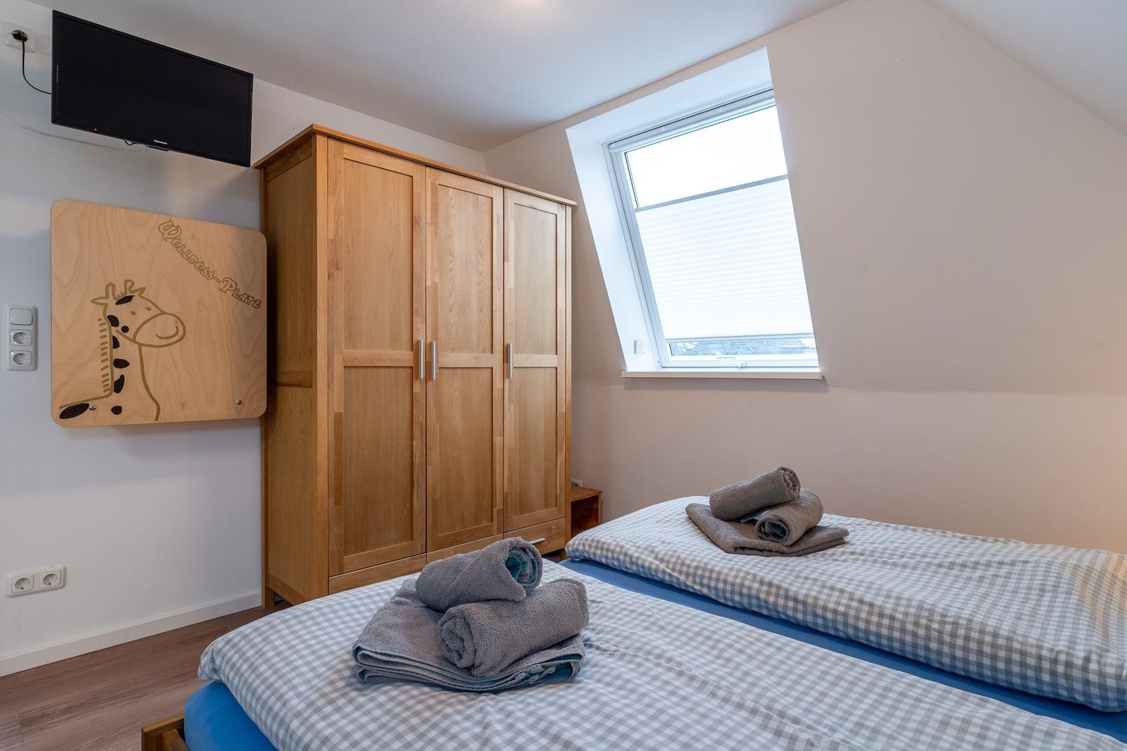 Zimmer mit zwei Betten, Kleiderschrank und Dachfenster. TV und Spielplatte an der Wand.