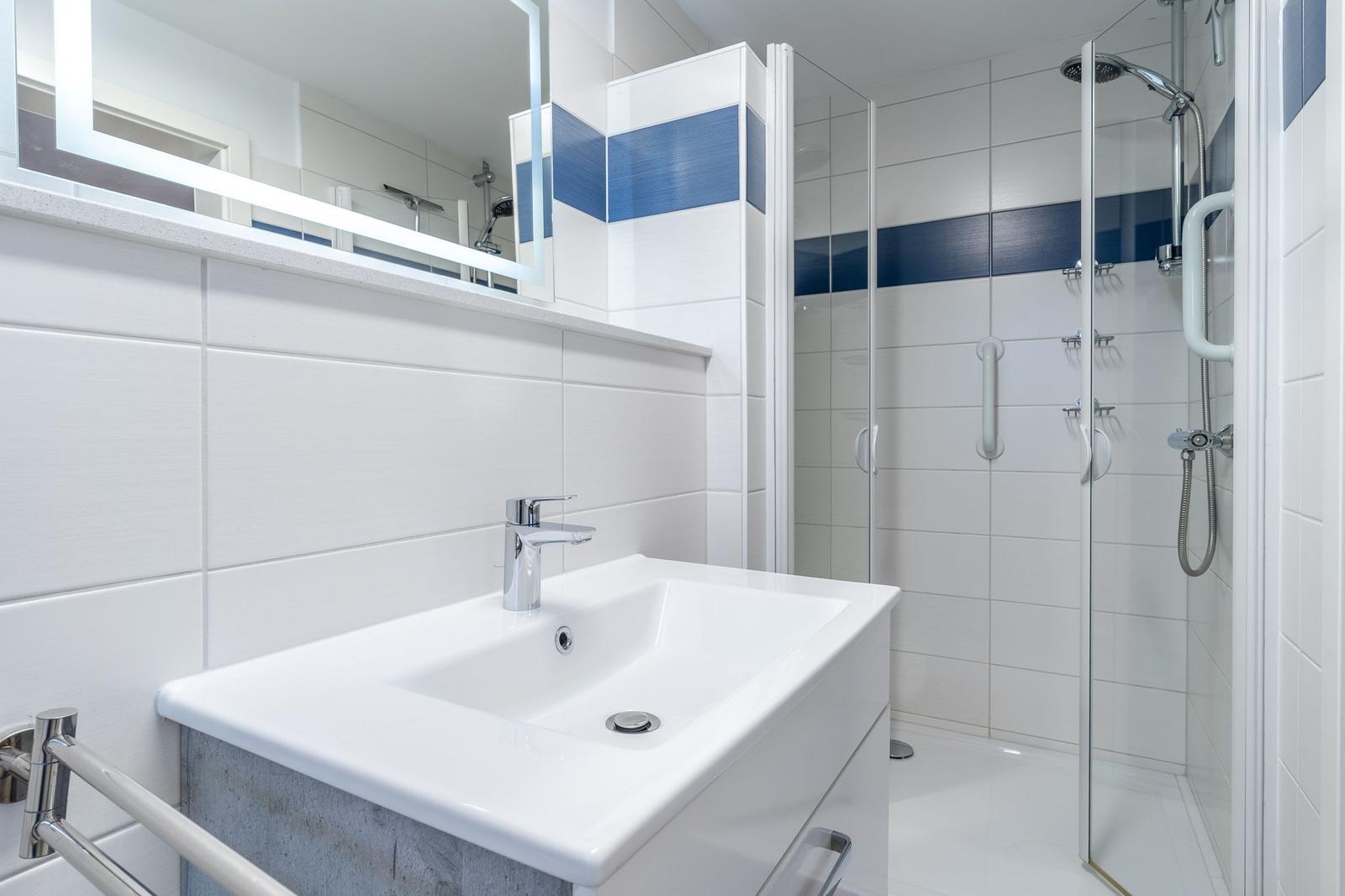 Badezimmer mit Dusche, Waschbecken und Spiegel.