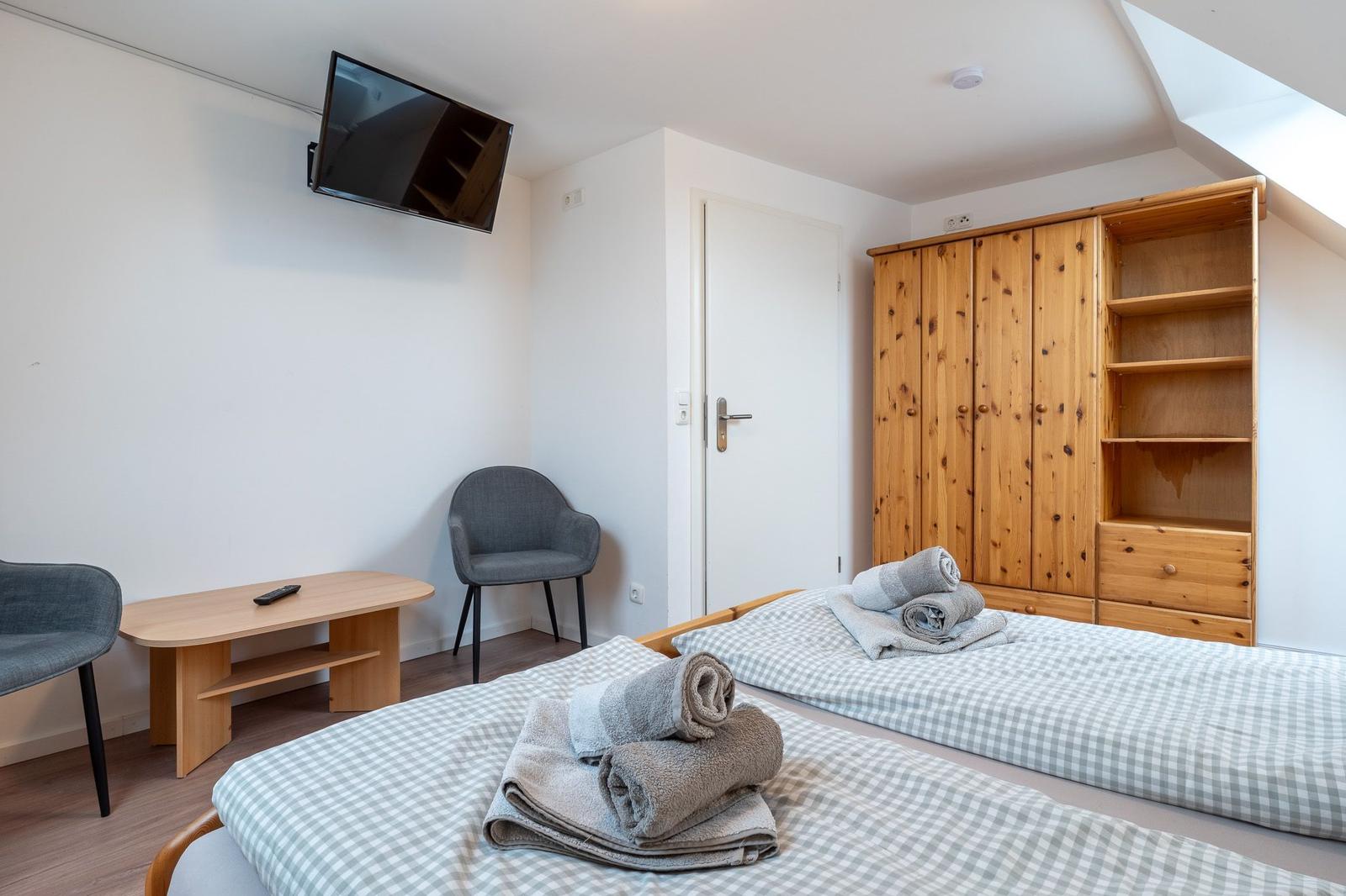 Zimmer mit Doppelbett, Holzschrank und Wand-TV.