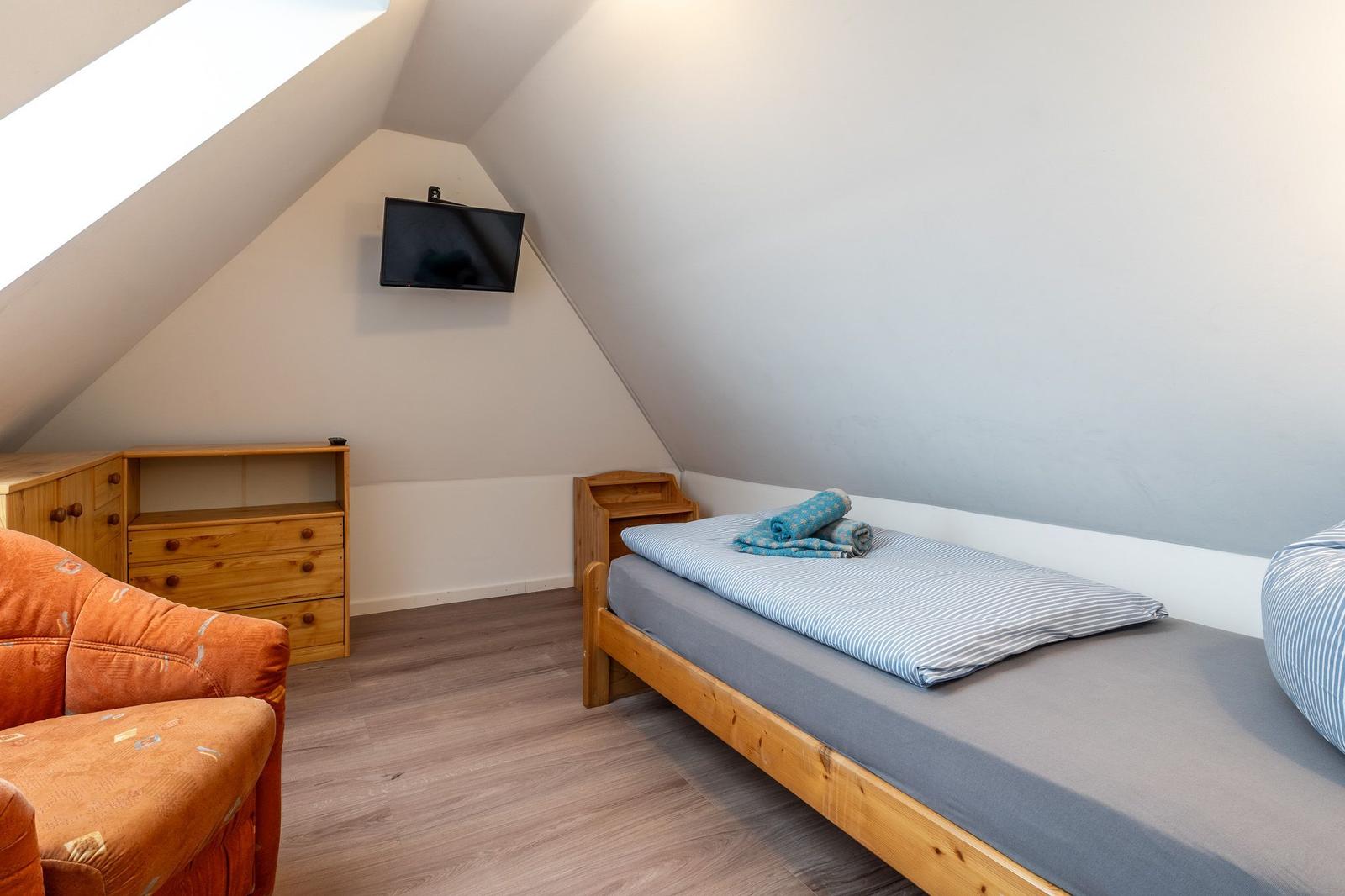 Zimmer mit Dachschrägen, Bett, Kleiderschrank und Wand-TV.