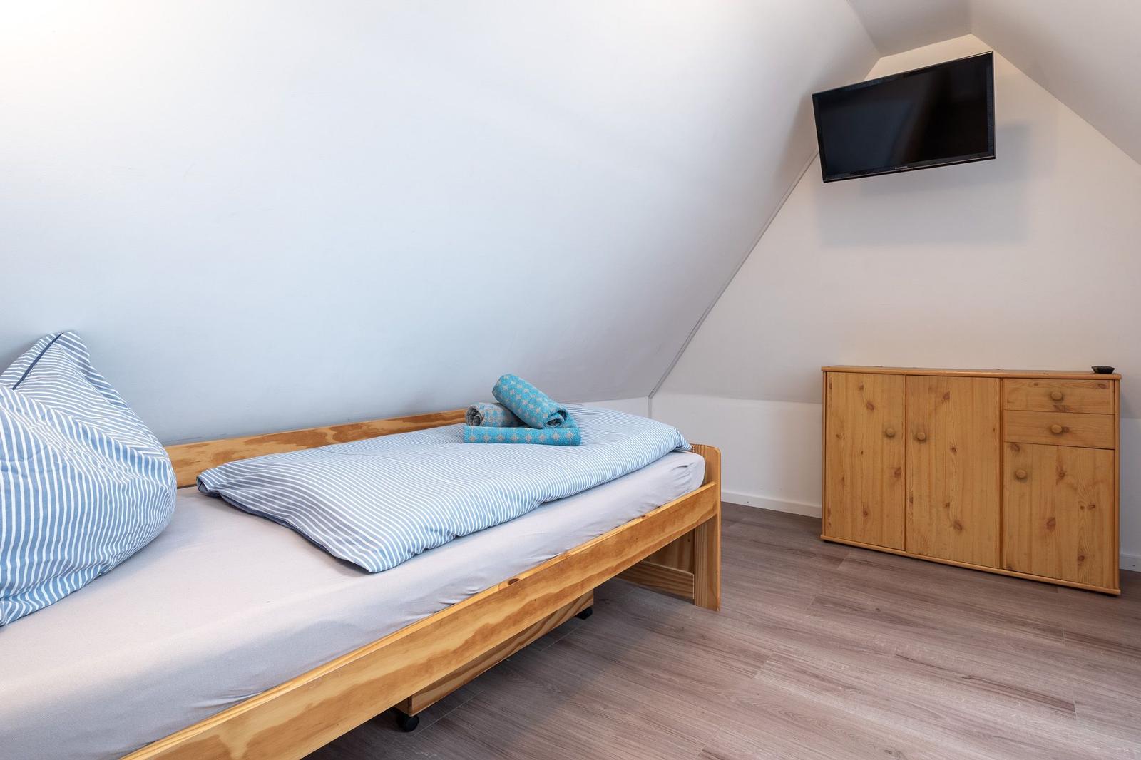Schlafzimmer mit Bett, Kleiderschrank und Fernseher an der Wand.