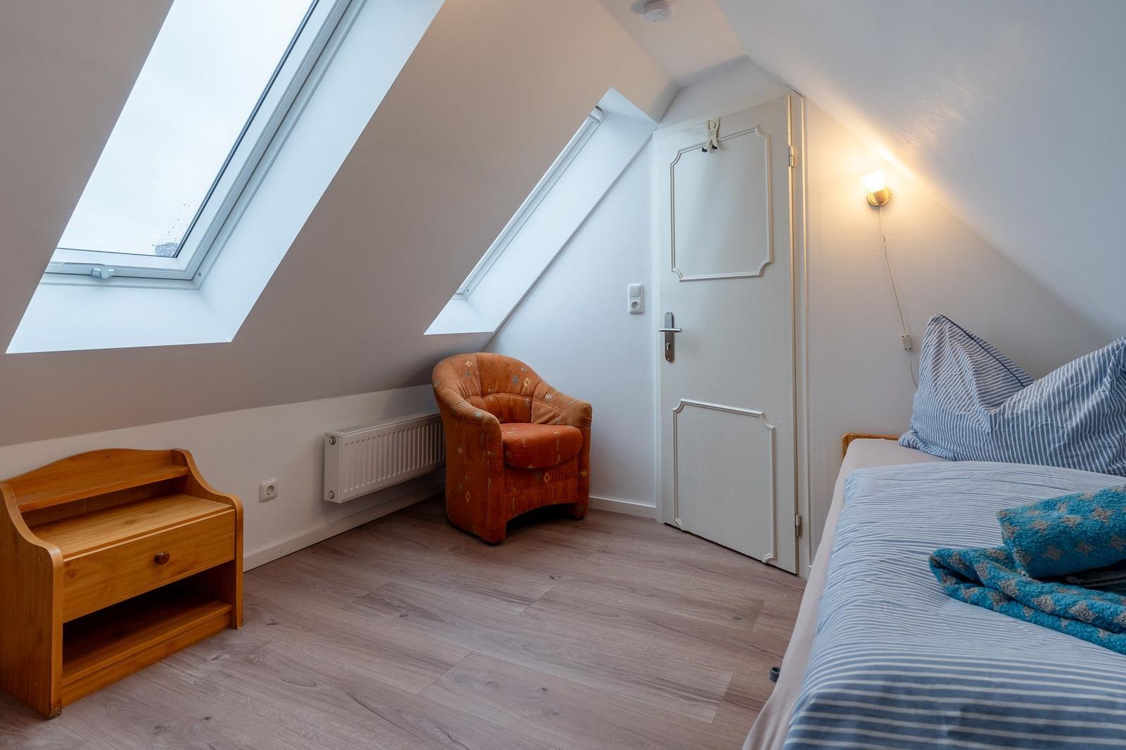 Dachgeschosszimmer mit Bett, Sessel und Dachfenster.