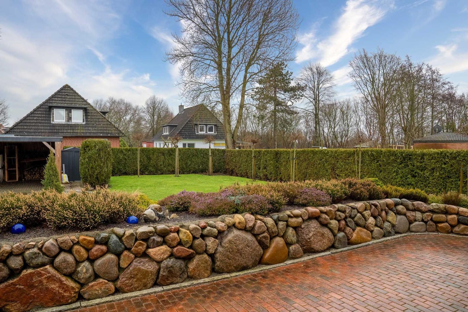 Haus mit Steinmauer, Rasen und Hecken im Garten