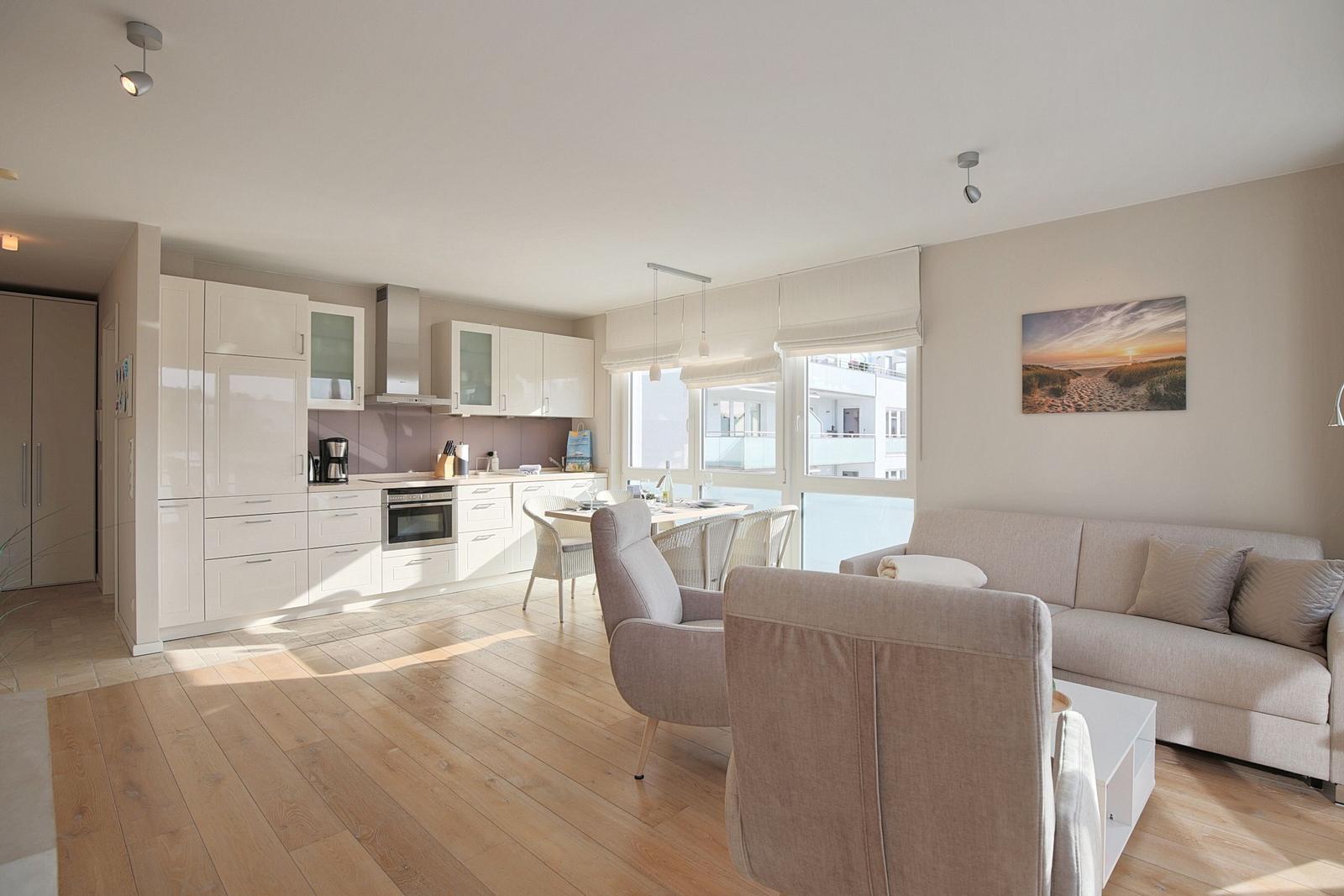 Wohn- und Essbereich mit Küche und großem Fenster. Sofa, Sessel und Tisch sind vorhanden.