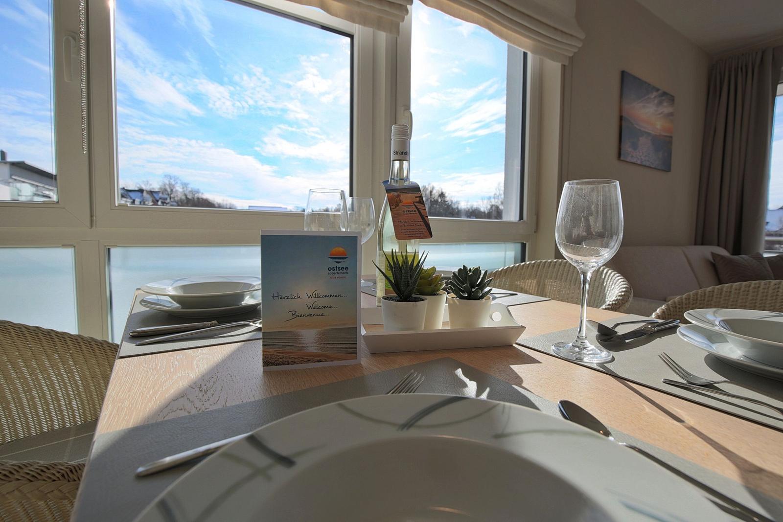 Gestellter Tisch mit Geschirr, Gläsern und Pflanzen vor großem Fenster mit Blick.