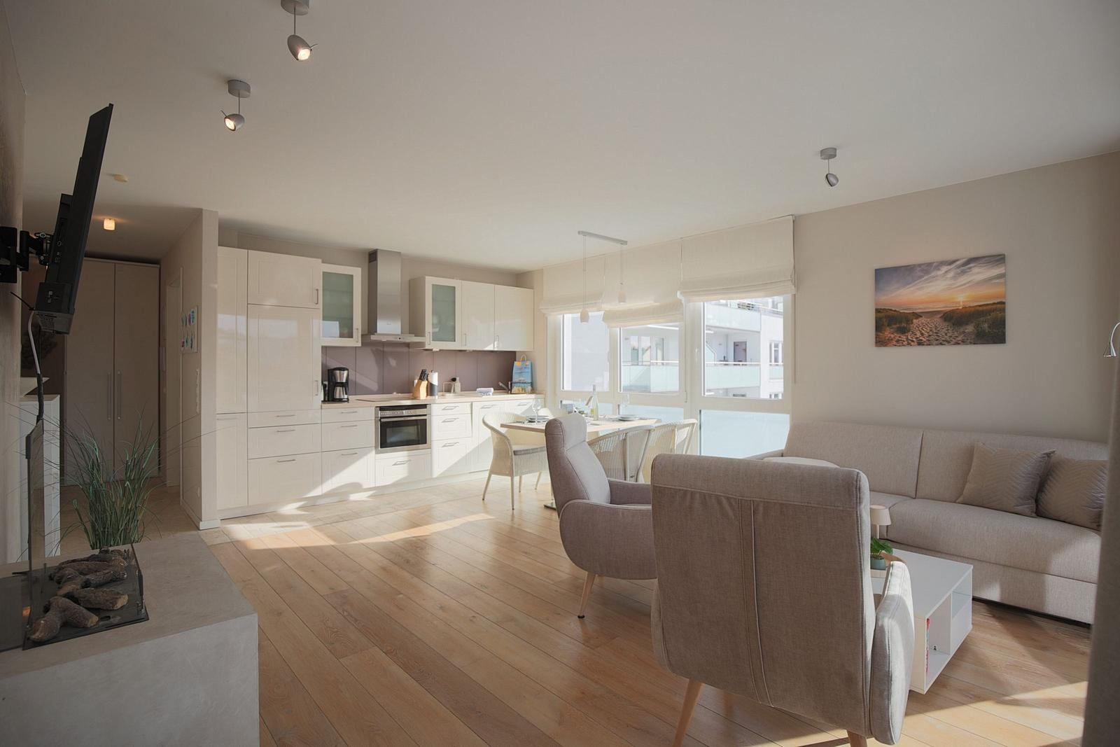 Wohn- und Küchenbereich mit Holzboden, Sofa, Stühlen und TV. Große Fenster mit Blick.
