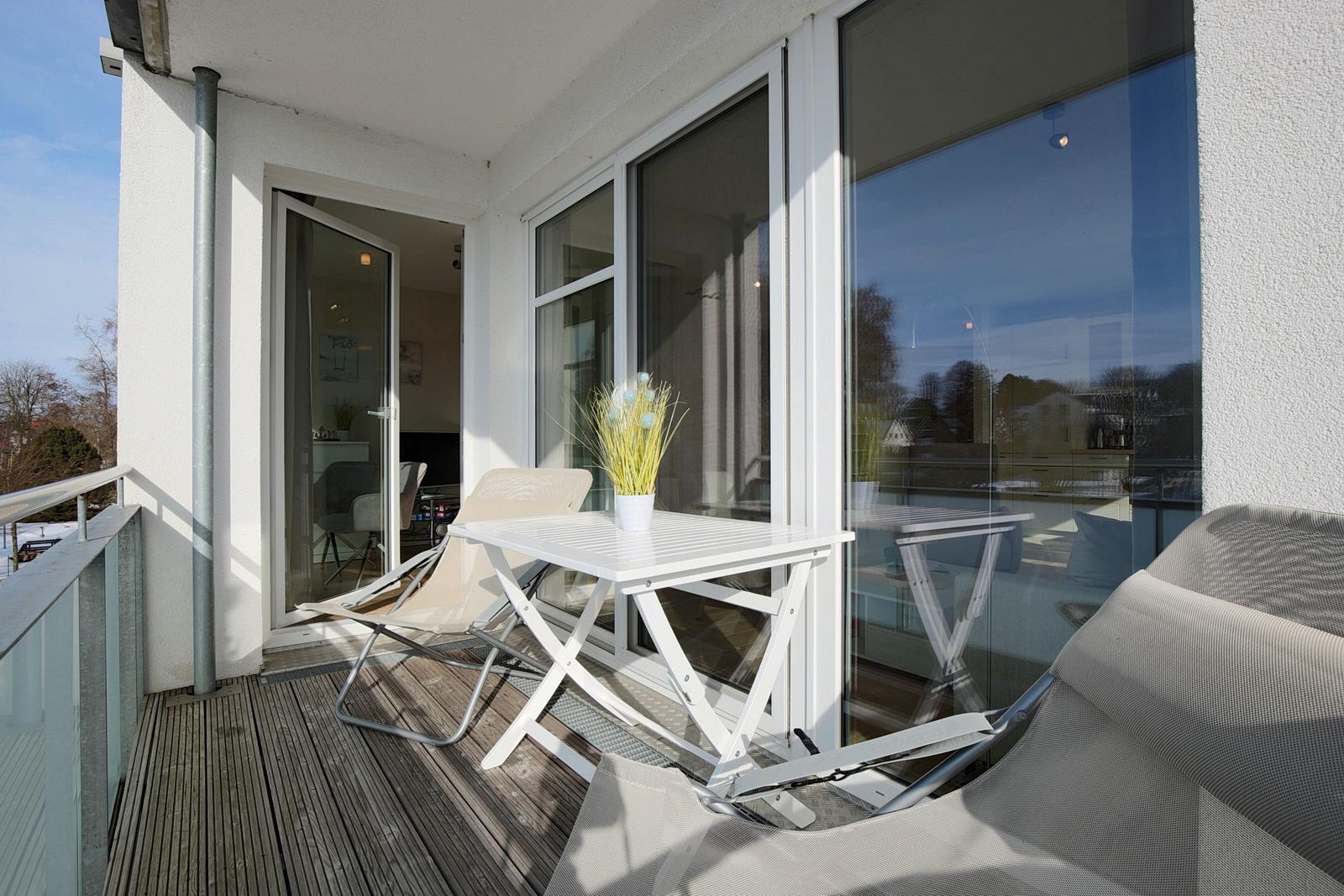 Terrasse mit Tisch, Stühlen und Pflanze. Glasfront führt ins Innere.