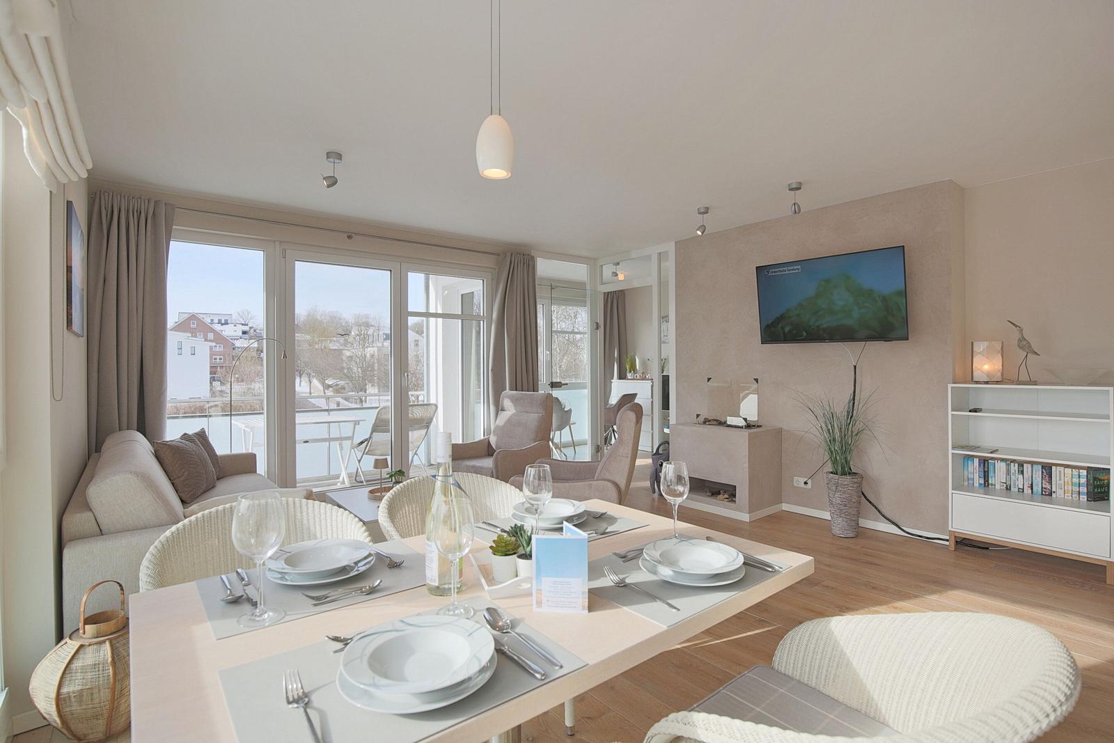 Essbereich mit Tisch und Stühlen, Fernseher und Balkonansicht.