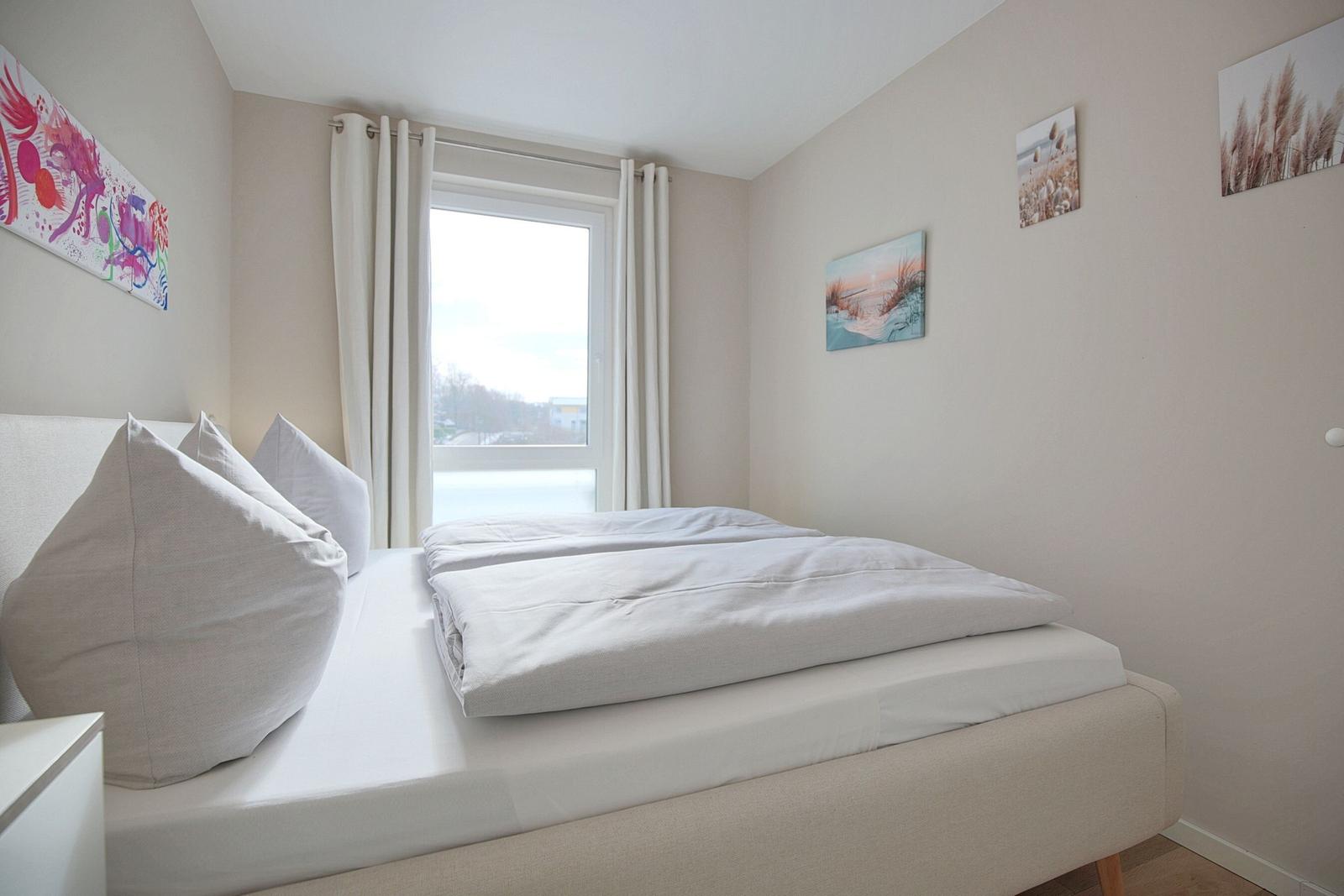 Schlafzimmer mit Bett, Fenster und Wandbildern.