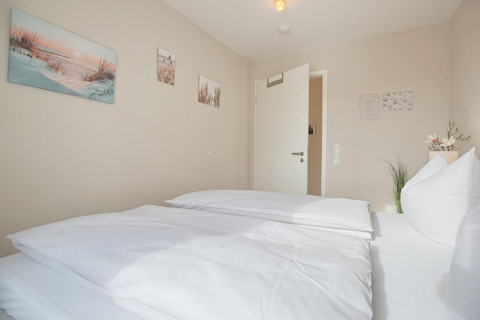 Schlafzimmer mit weißem Bett, Wandbildern und Pflanzen.