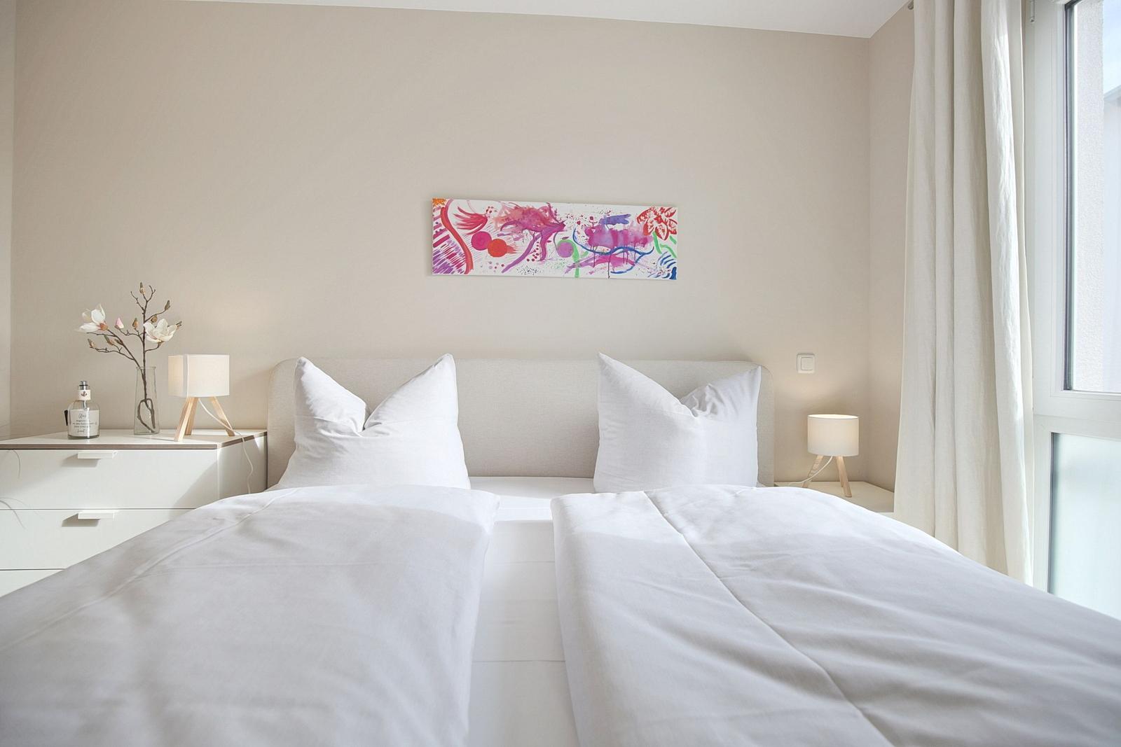 Schlafzimmer mit Doppelbett, Nachttischen und Fenster. Wandbild über dem Bett.