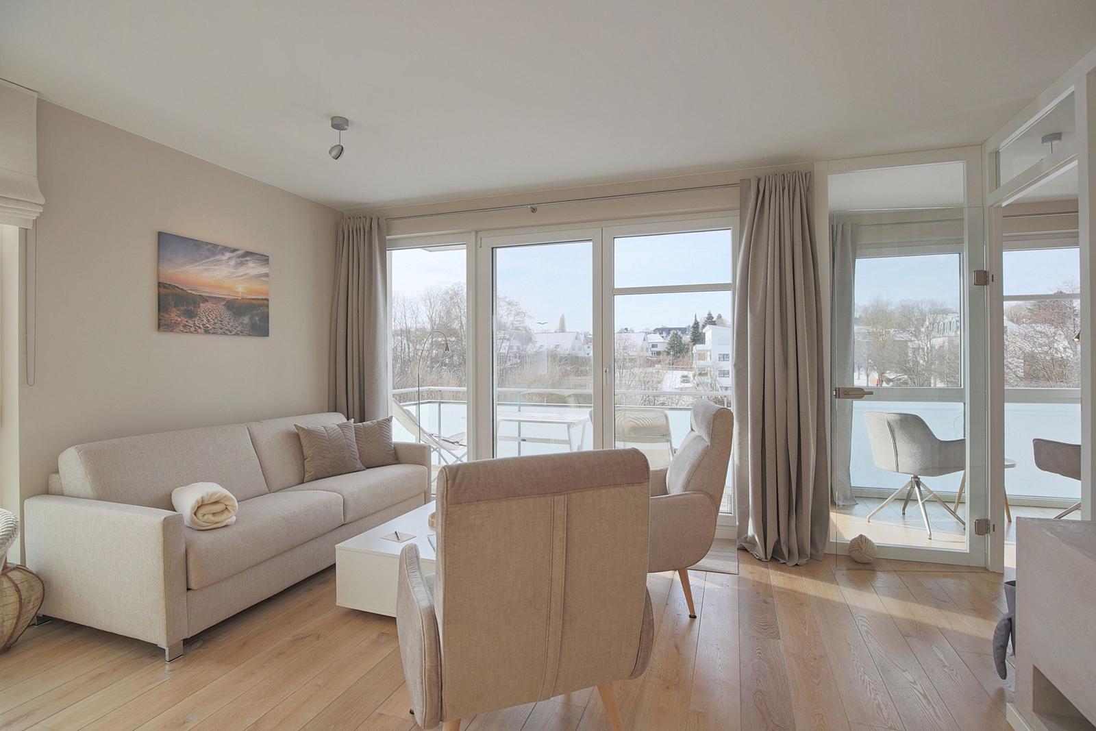 Wohnzimmer mit Sofa, Sessel und Blick auf Balkon