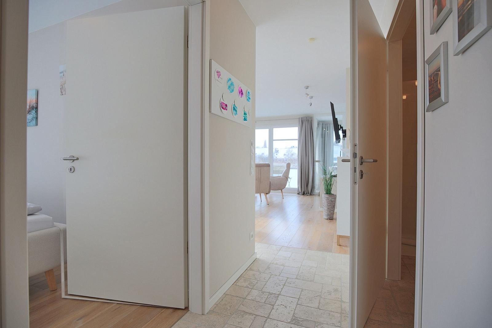 Flur mit Tür zu Schlafzimmer und Blick in Wohnbereich mit Fenster und Pflanze.