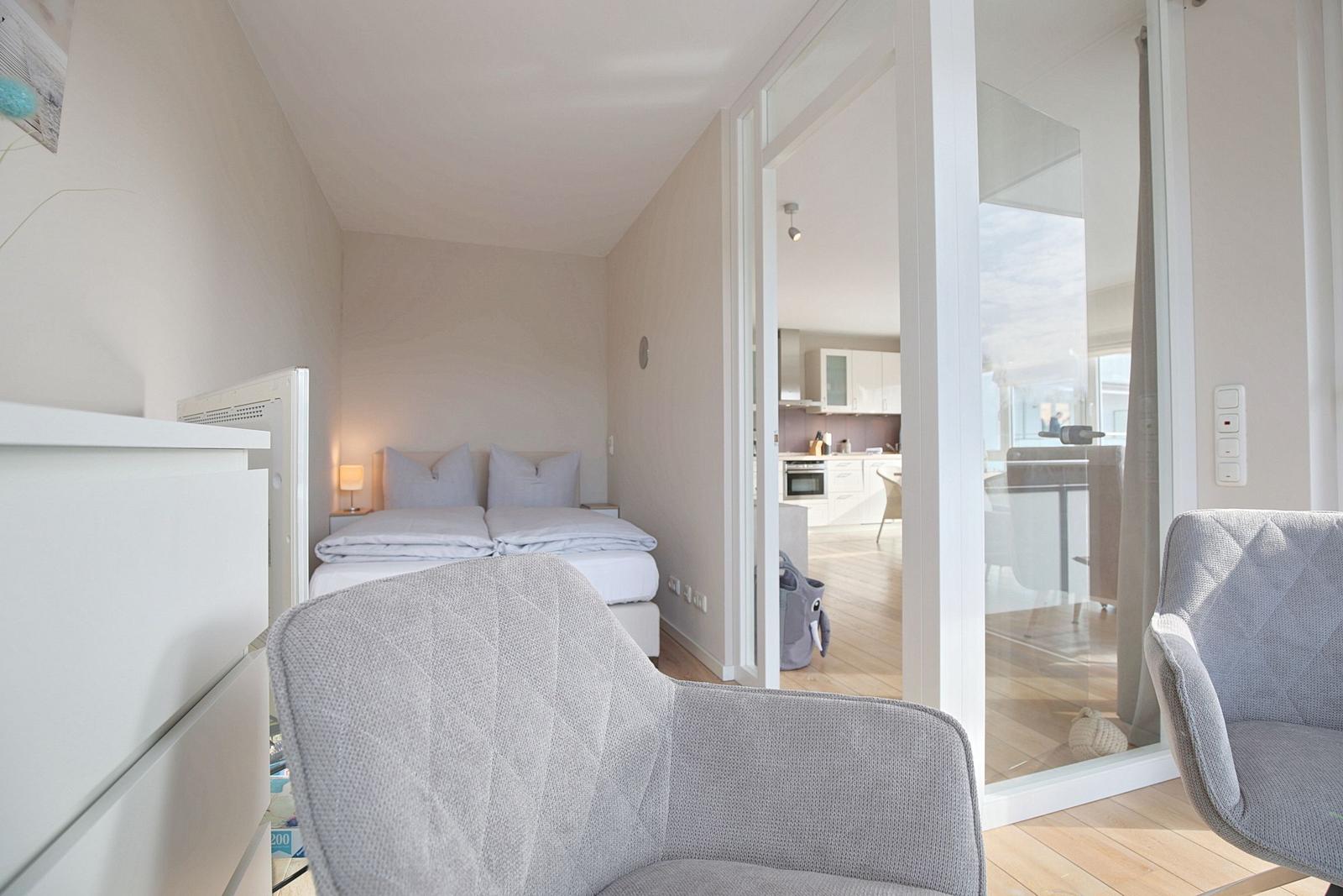 Schlafzimmer mit Bett und Sessel, Blick in Küche und Wohnbereich.