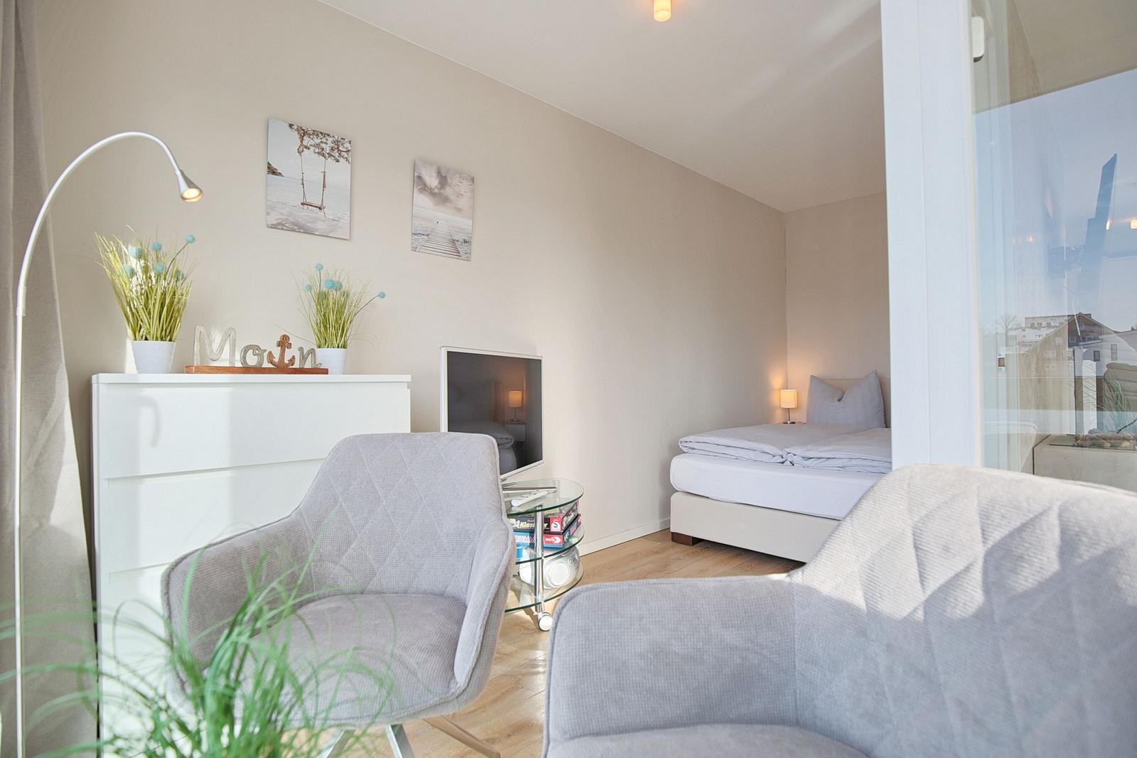 Ein Schlafzimmer mit Bett, zwei Sesseln und Fernseher. Fenster mit Blick nach draußen.