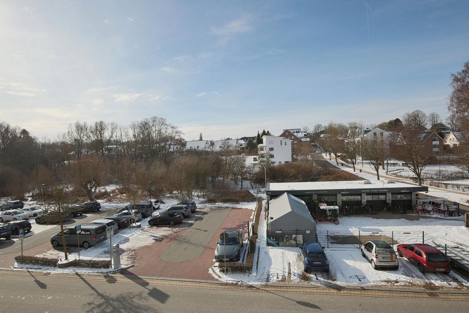 Schneebedeckter Parkplatz mit Fahrradverleih und Wohnhäusern im Hintergrund.