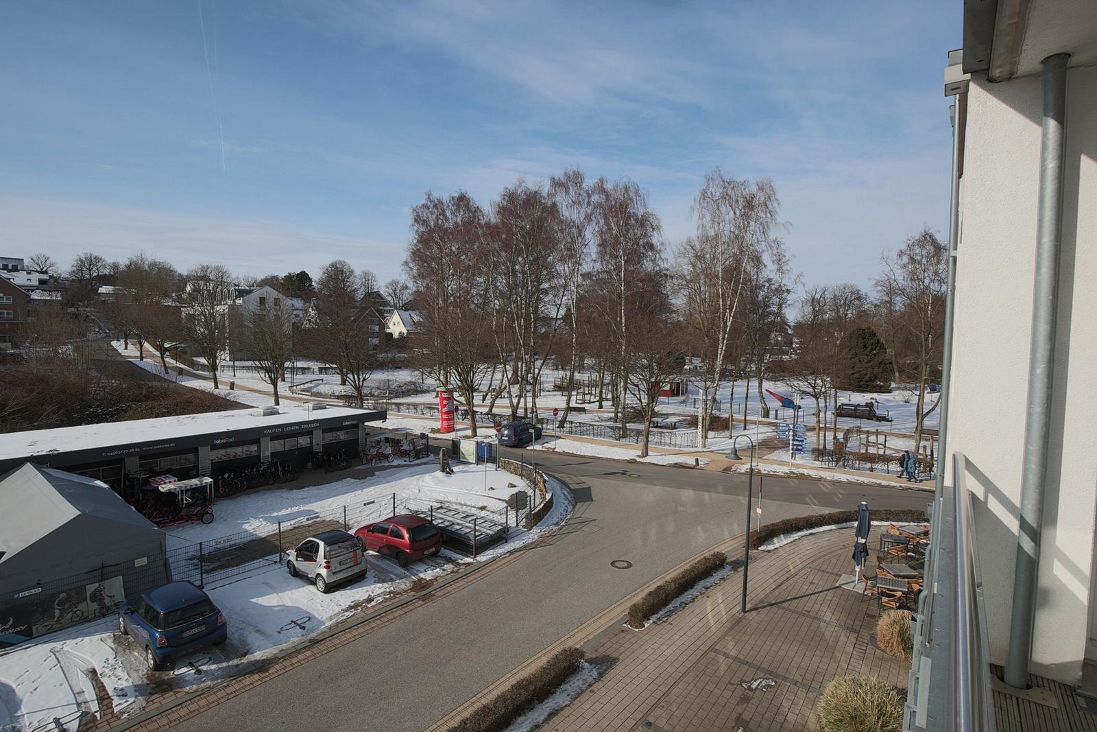 Blick auf verschneite Straße mit Bäumen und Parkplatz.