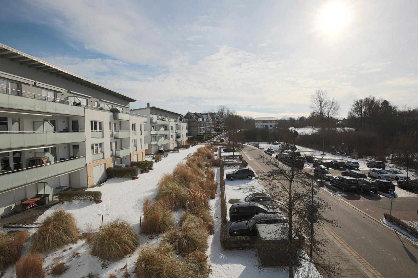 Winterlicher Blick auf Wohngebäude und Parkplatz mit Schnee und Bäumen.