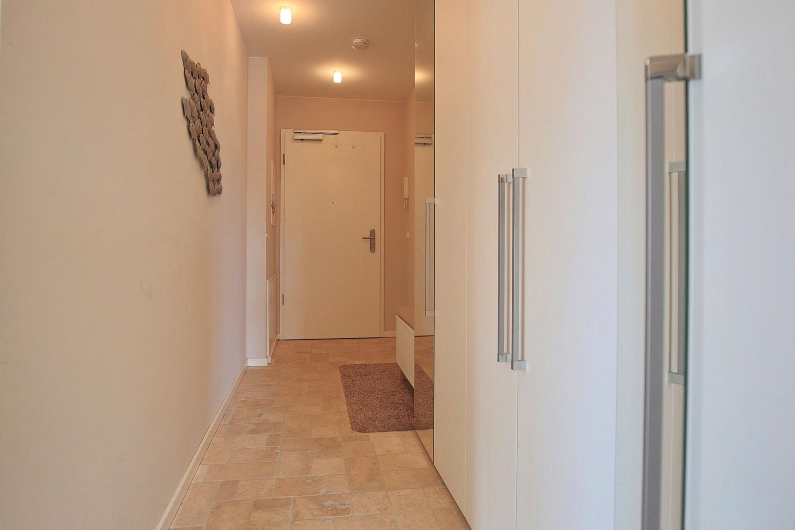 Flur mit Fliesenboden, weißen Schränken und Wanddekoration.