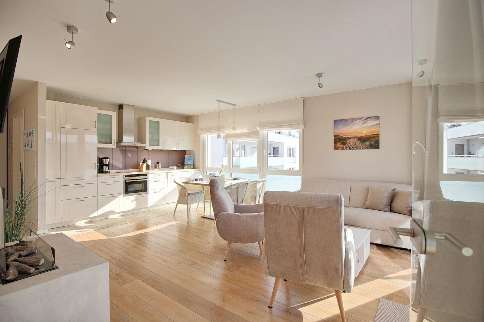 Wohn- und Essbereich mit Küche, Sofa und Stühlen. Holzboden und große Fenster.