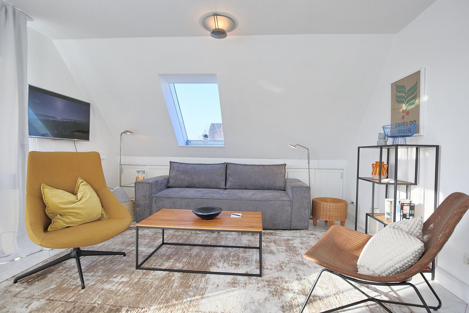 Wohnzimmer mit grauem Sofa, gelber Sessel und Holztisch unter Dachschräge.