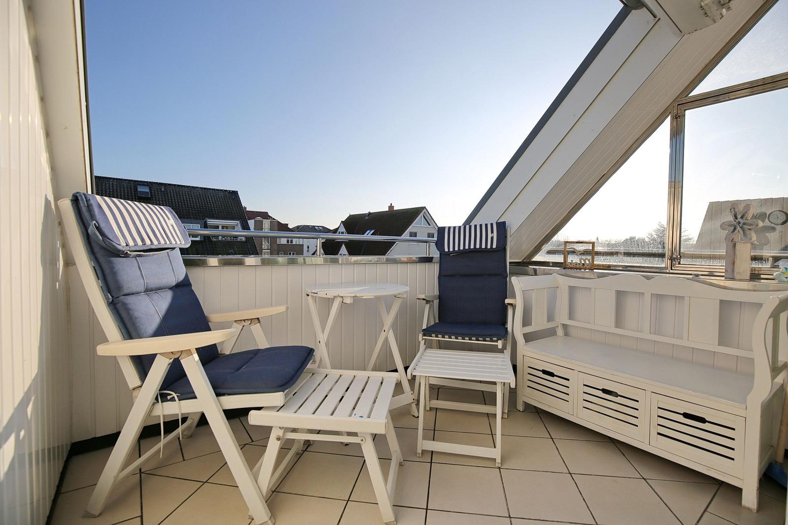Terrasse mit zwei blauen Sesseln, Tisch und Bank. Blick auf Wohnhäuser und Himmel.