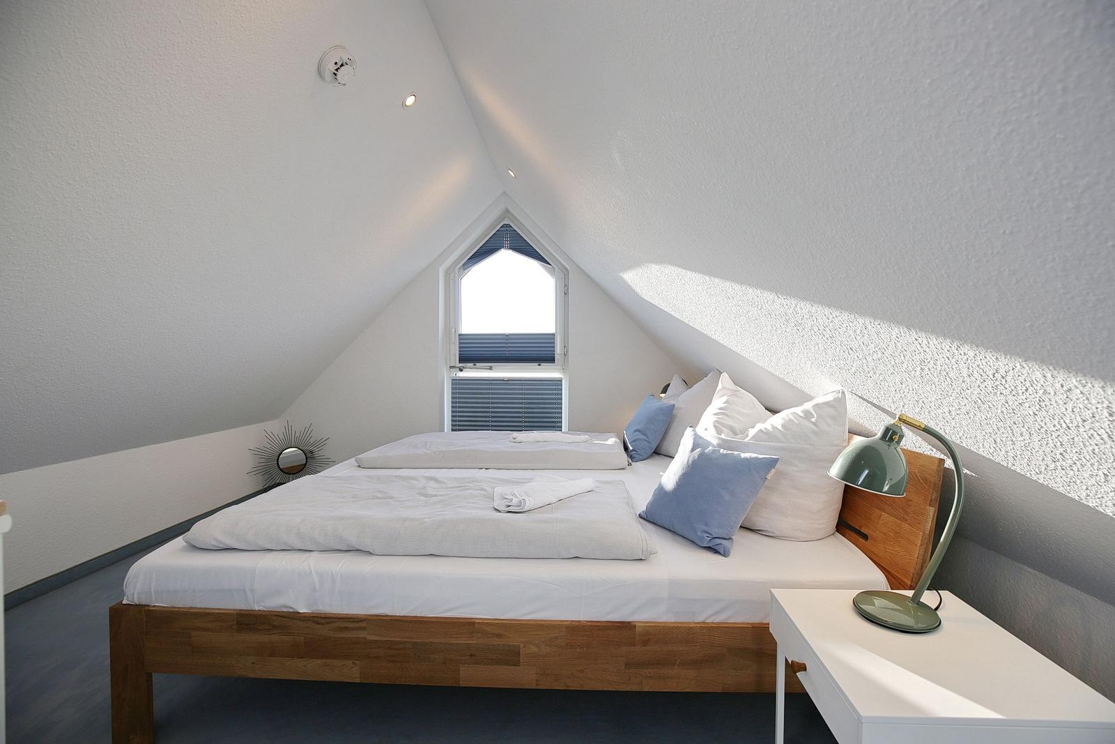 Schlafzimmer mit Dachschrägen, Bett, Nachttisch und Fenster