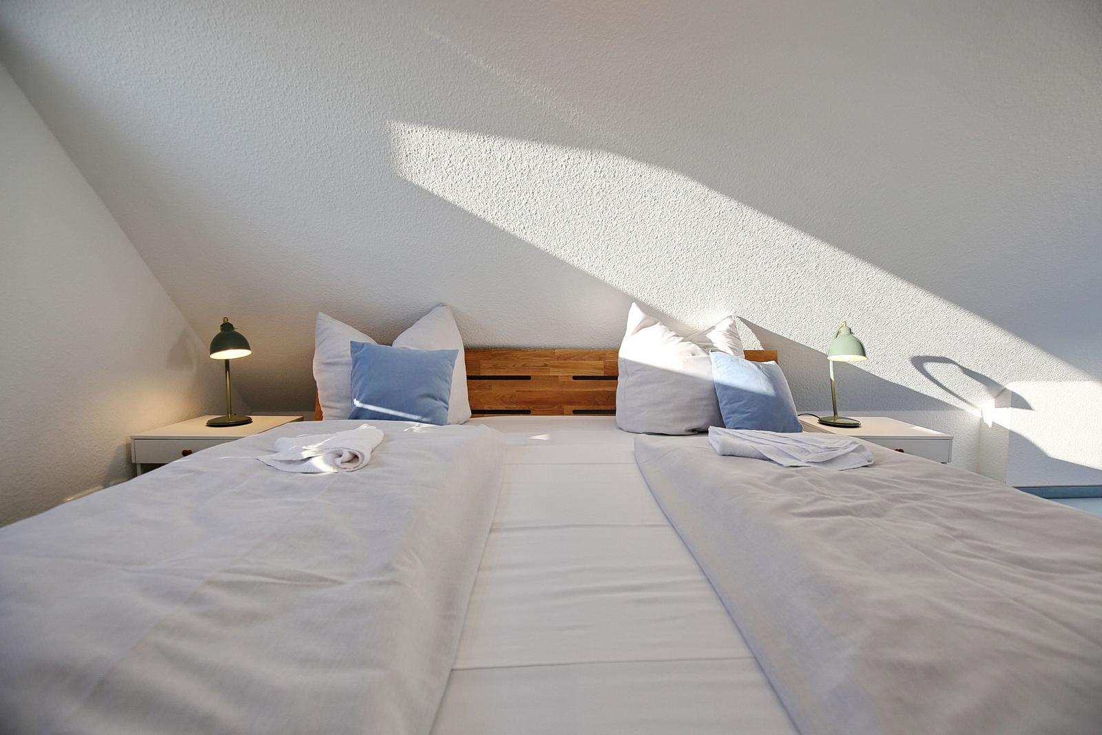 Zimmer mit Doppelbett, Holzkopfteil und zwei Nachttischen mit Lampen.