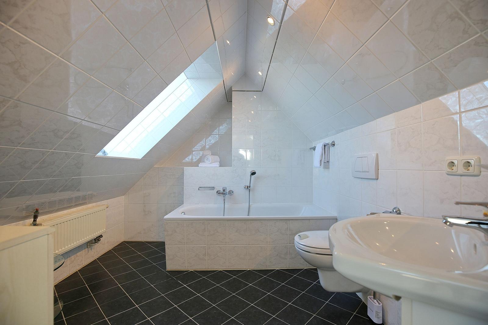 Badezimmer mit Dusche, Badewanne, Waschbecken und Toilette unter Dachschrägen mit Dachfenster.