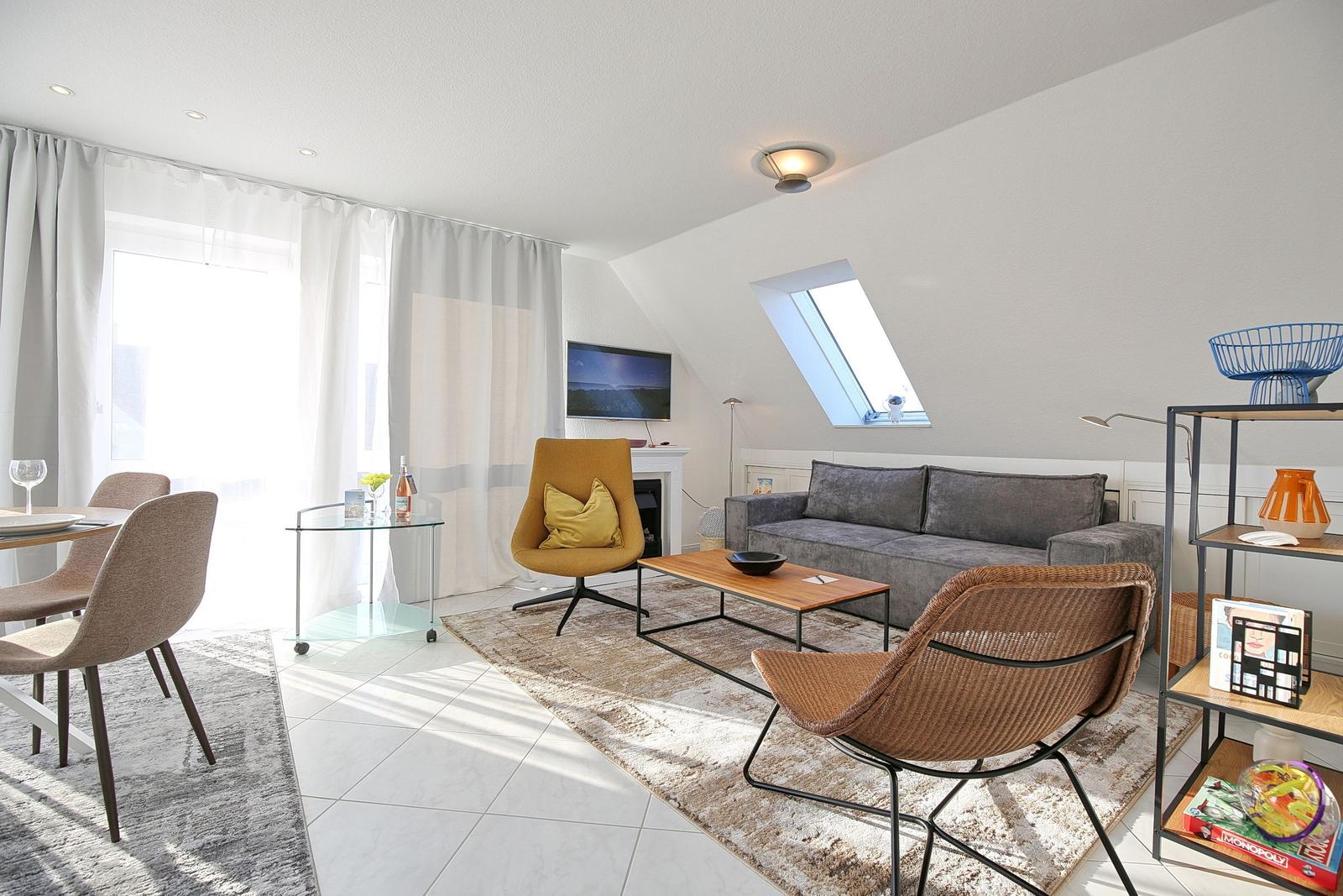 Wohn- und Essbereich mit Sofa, Sessel und TV. Dachfenster und große Fenster.