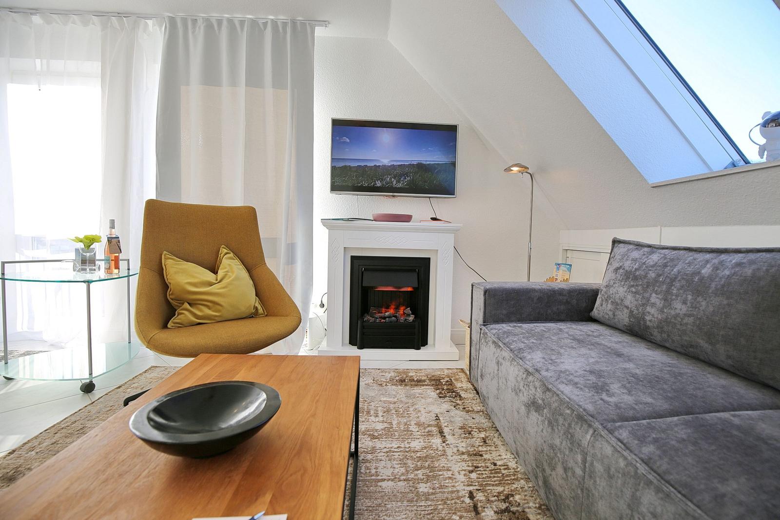 Wohnzimmer mit Sofa, Sessel, Kamin und TV unter Dachschrägen.