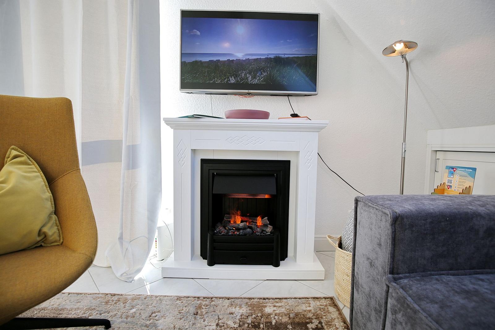 Wohnzimmer mit Kamin, Fernseher und Sitzgelegenheiten.