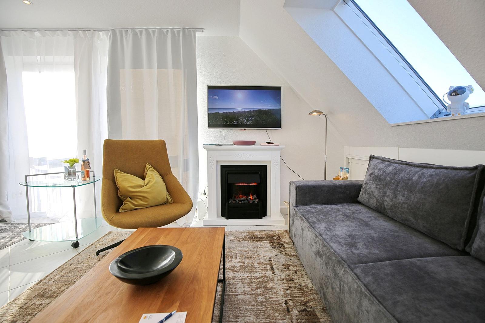 Wohnzimmer mit Sofa, Sessel, Fernseher und Kamin