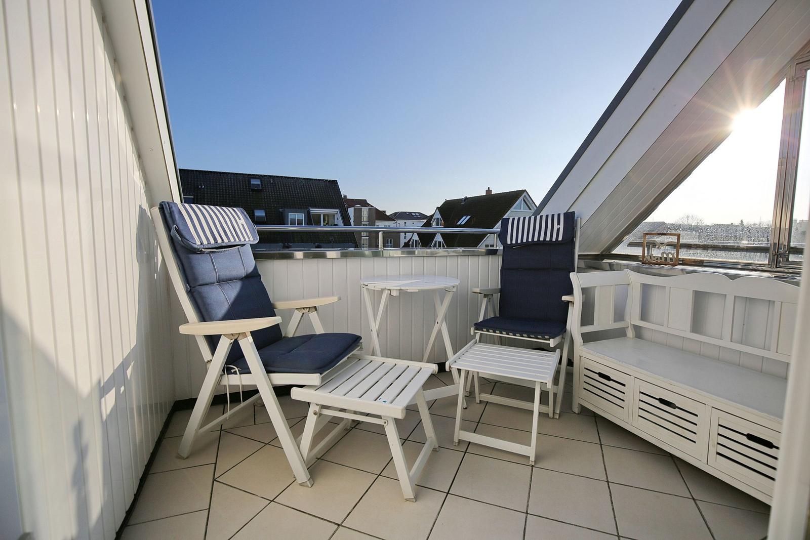 Terrasse mit zwei blauen Sesseln, Tisch und Bank. Blick auf Dächer und Wasser.