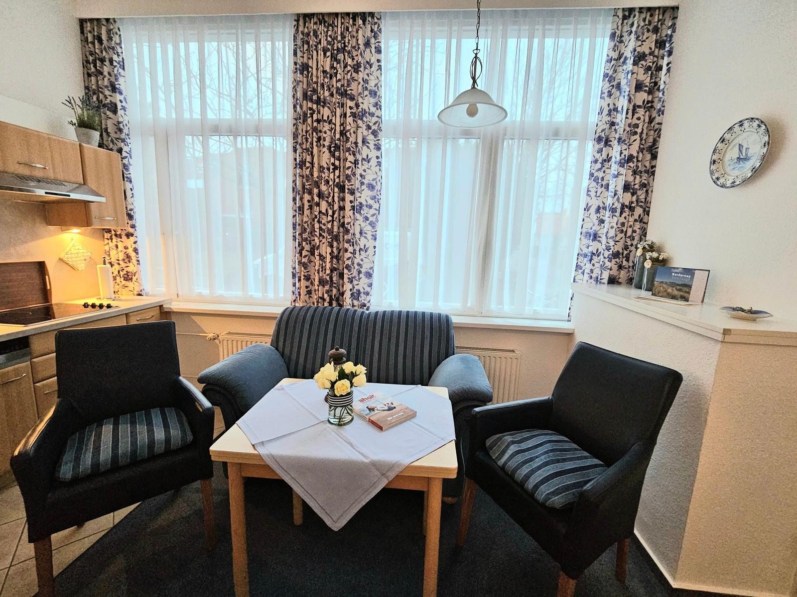 Ein Essbereich mit Tisch, zwei Stühlen und einem Sofa vor großem Fenster.