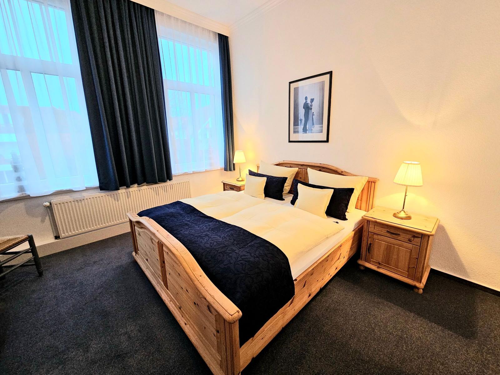 Schlafzimmer mit Holzbett, zwei Nachttischen und großen Fenstern.