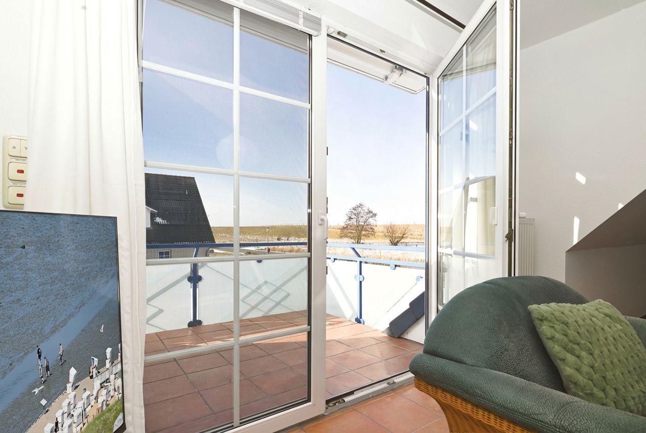 Glasfenster führen auf eine Terrasse mit Blick auf Felder und ein Haus.