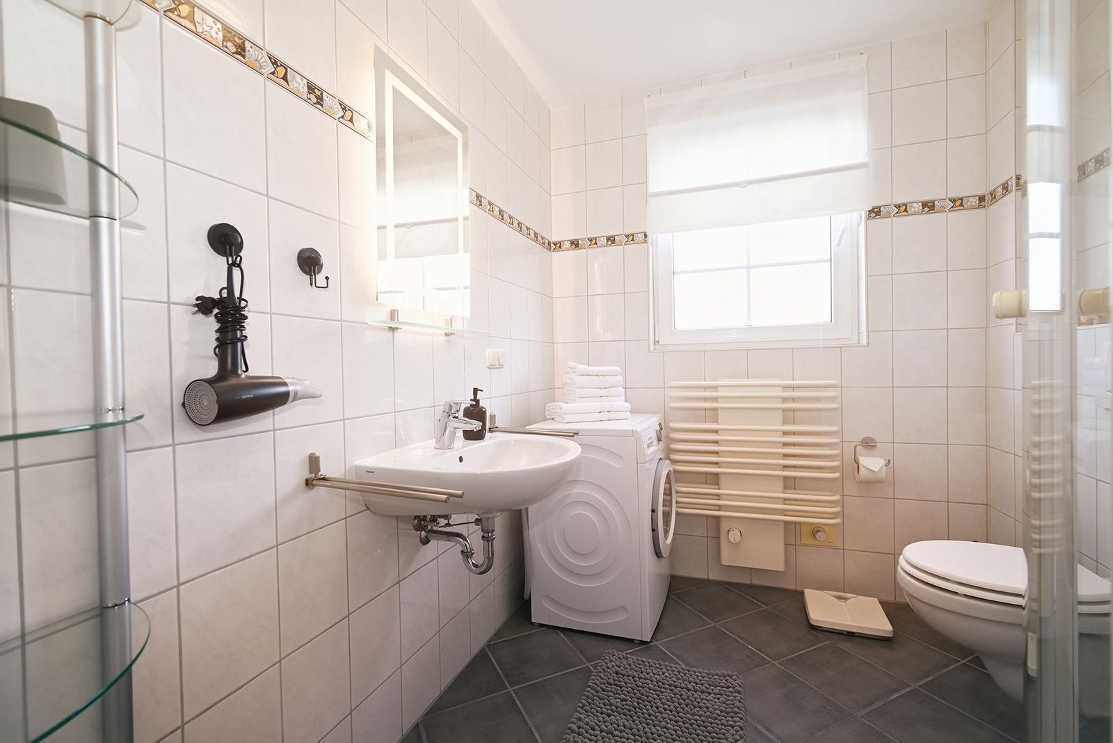 Badezimmer mit Waschmaschine, WC, Spiegel und Fenster.