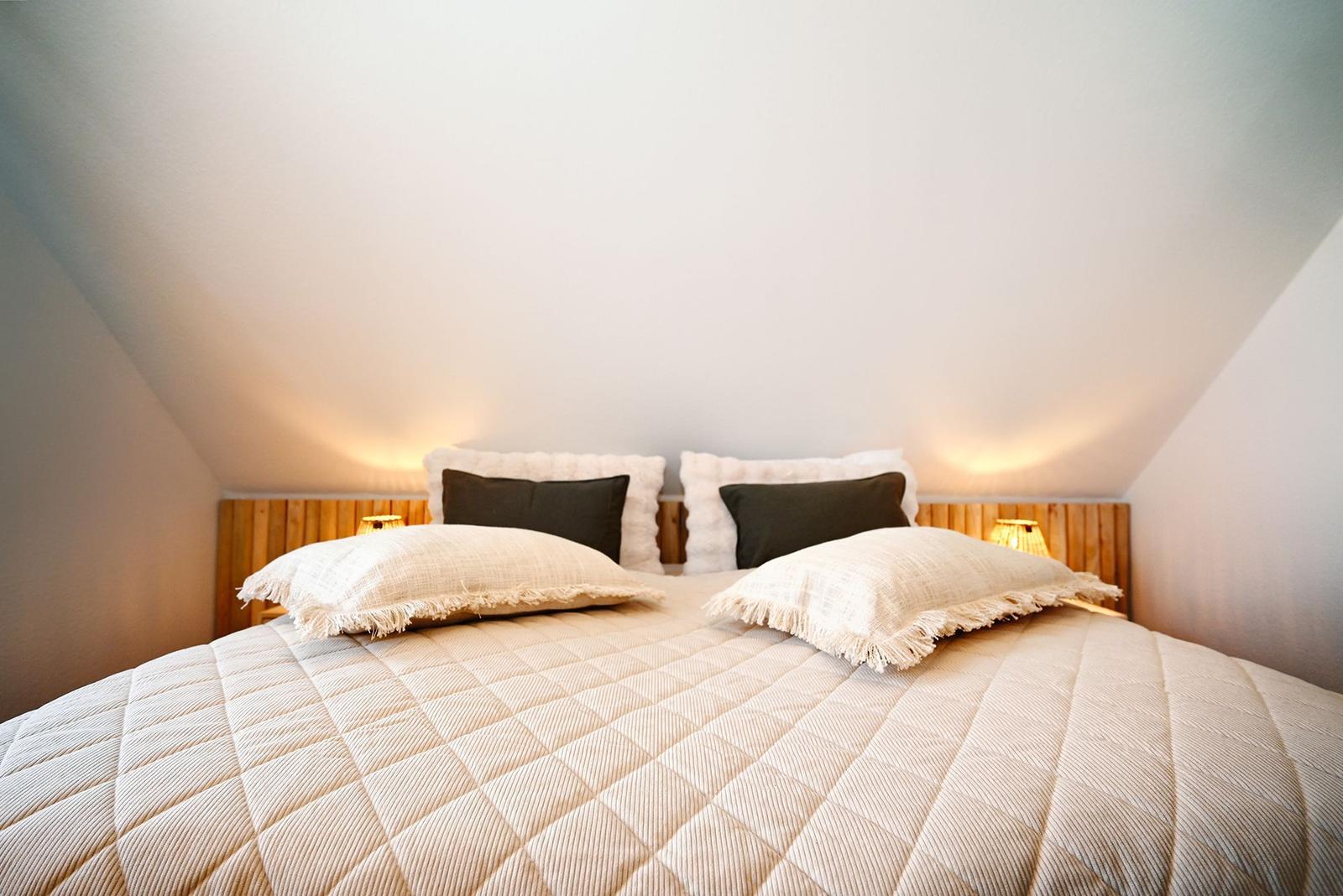 Schlafzimmer mit Bett, Kissen und Holz Kopfteil unter schrägen Decken.