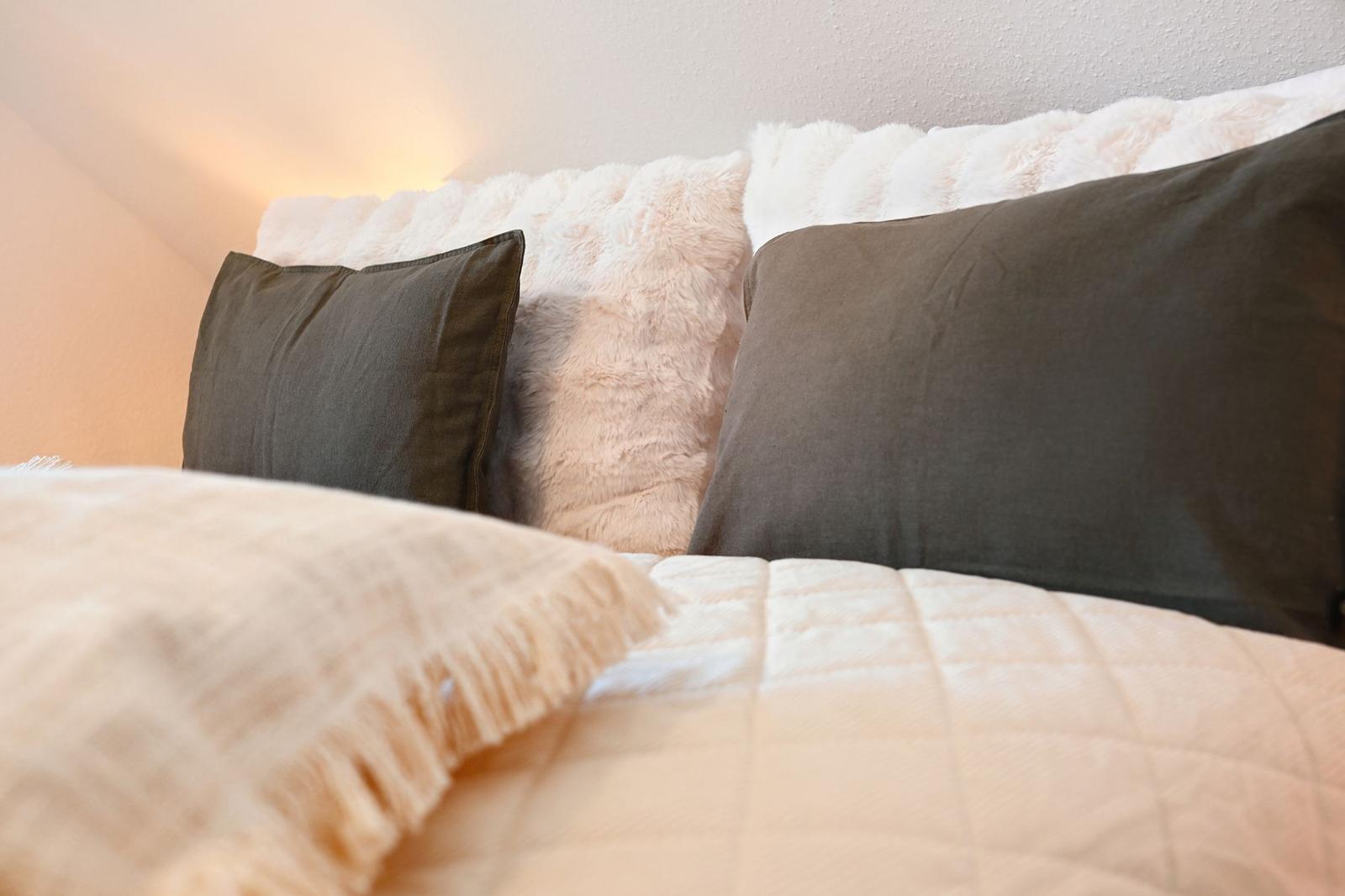 Bettkopf mit Fellkissen und grauen Kissen