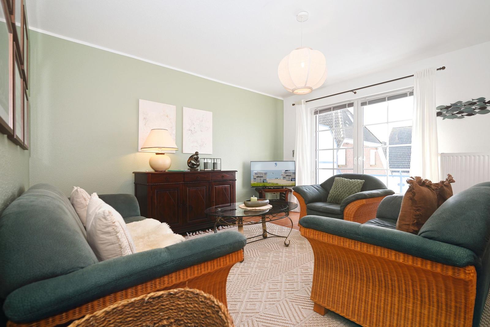 Wohnzimmer mit Sofa, Sessel und Fernseher. Fenster mit Blick nach draußen.