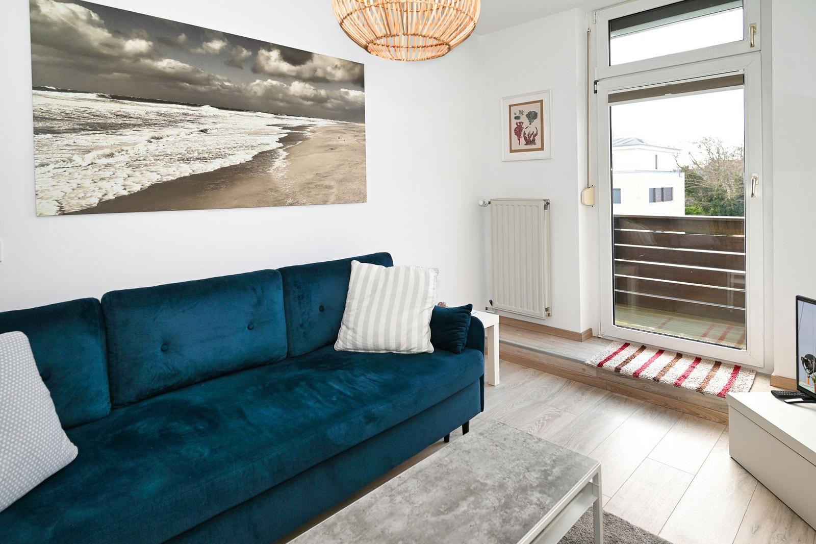 Ein Wohnzimmer mit blauem Sofa, Glas-Tür und Wandbild