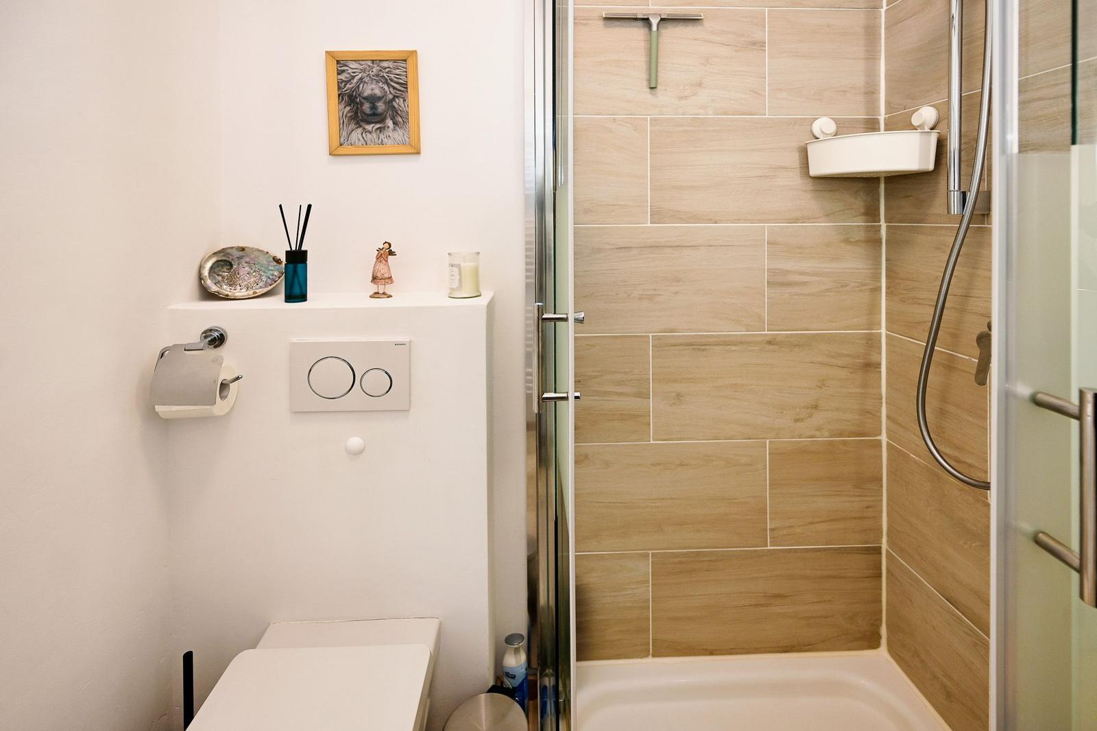 Bad mit Dusche, Toilette und kleinen Dekorationsgegenständen an der Wand.